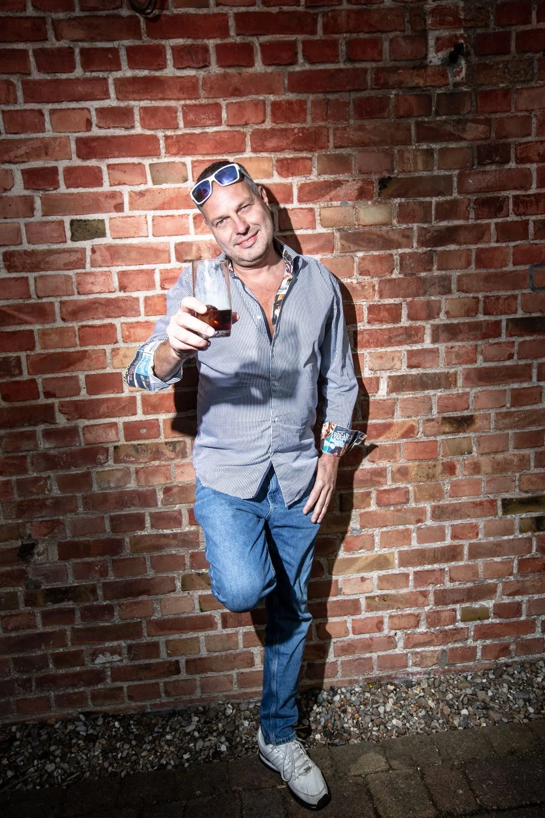 Tommy mit einem Glas vor einer Backsteinwand